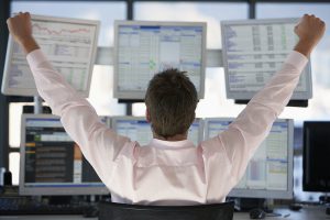 Rear view of stock trader with hands raised looking at multiple